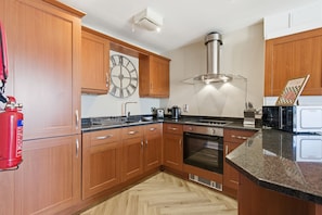 Una cocina con armarios de madera, campana extractora de acero inoxidable, un reloj y un extintor.