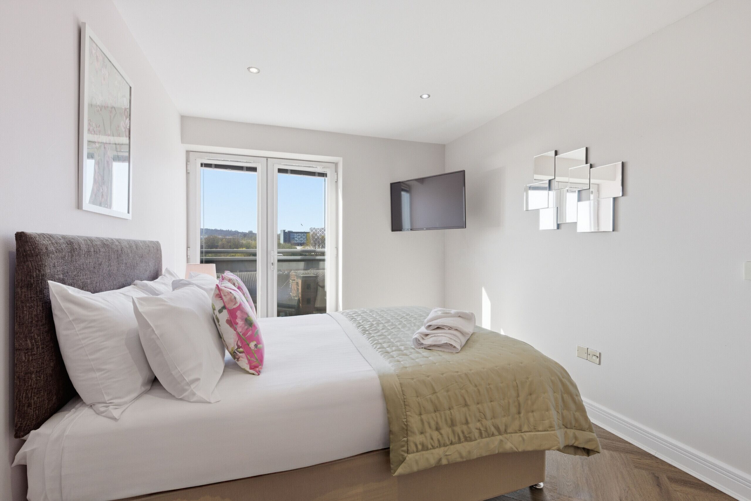 A bedroom with a bed, a TV, a window, and a wall-mounted mirror.