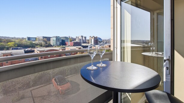 A balcony with a table, two wine glasses, and a city view. - Properties Unique | The Peak (Newcastle Upon Tyne)