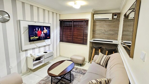 A living room with a TV, sofa, coffee table, and a small side table. - The Leneade - Exquisite Apt.1 (City Centre/Wuse 2) (Abuja)