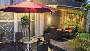 An outdoor patio with a round table and chairs, a red umbrella, and potted plants. - The Leneade - Exquisite Apt.1 (City Centre/Wuse 2) (Abuja)