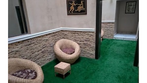 A corner room with a stone wall, two wicker chairs, a small stool, and a green carpet. - The Leneade - Exquisite Apt.1 (City Centre/Wuse 2) (Abuja)