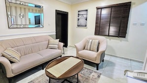 A living room with a beige sofa, a matching armchair, a small coffee table, a mirror, and a framed picture on the wall. - The Leneade - Exquisite Apt.1 (City Centre/Wuse 2) (Abuja)