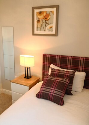 Cozy retreat with a plaid headboard and matching pillows, a bedside table, and a framed artwork above the bed.