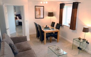 Relax in this stylish living room with a glass-top dining table, comfortable sofa, and a beautiful abstract painting.