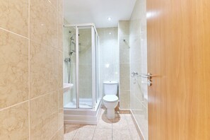 Bathroom features a glass-enclosed shower with handheld showerhead and wall-mounted faucet, a standard toilet, and a tiled floor.