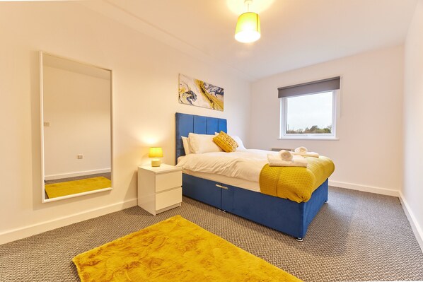 Relax in this serene bedroom with a large bed, matching nightstand, and a large window offering a view of the outdoors.