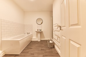 Bathroom features a bathtub, pedestal sink, and wicker basket.
