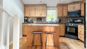 A modern kitchen with wooden cabinets, a large island with stools, a built-in oven, and a microwave. - Downtown Douglas-Craftsman Charm-Sleeps 6 (Douglas)