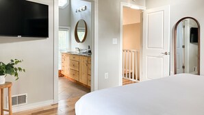 A bedroom with a bed, a TV, and a bathroom with a sink and mirror. - Downtown Douglas-Craftsman Charm-Sleeps 6 (Douglas)