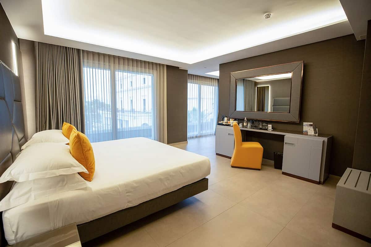 Ein modernes Hotelzimmer mit einem großen Bett, einem Schreibtisch, einem Sessel und einem Spiegel.