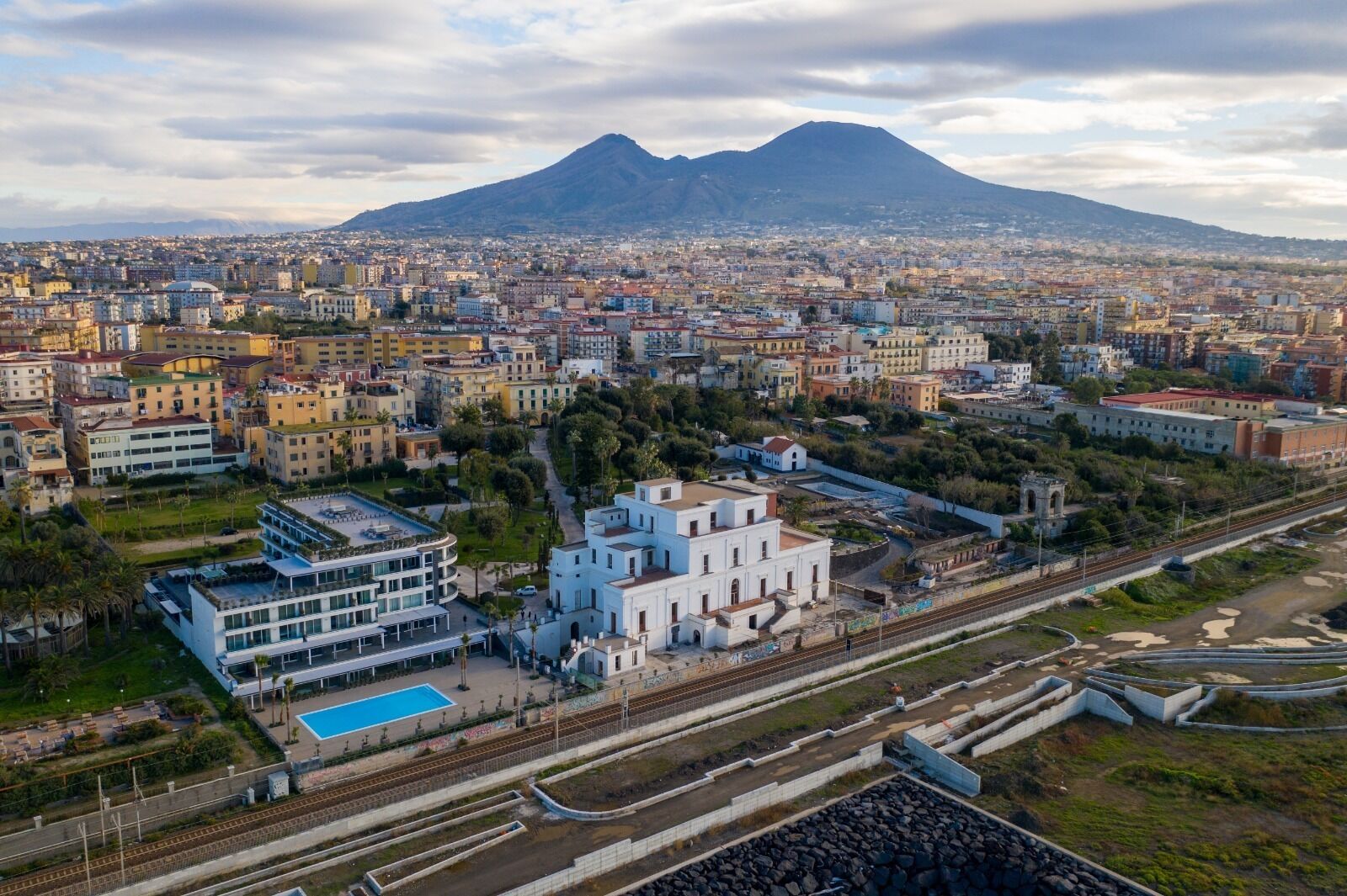 An aerial view of a city with a prominent mountain in the background, a mix of residential and commercial buildings, and a railway track running through the center.