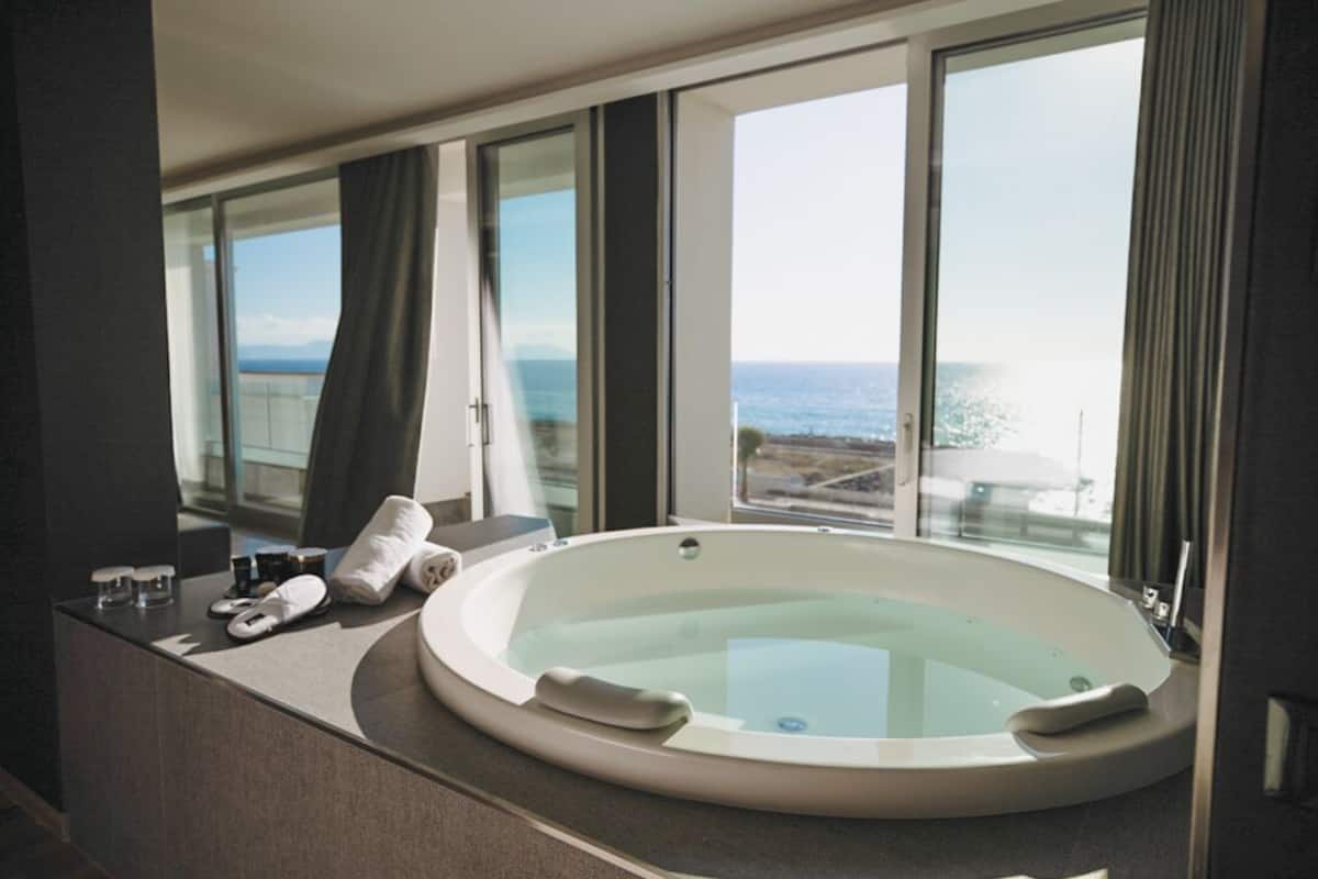Ein modernes Badezimmer mit einer großzügigen Badewanne, einem Waschtisch und Meerblick.