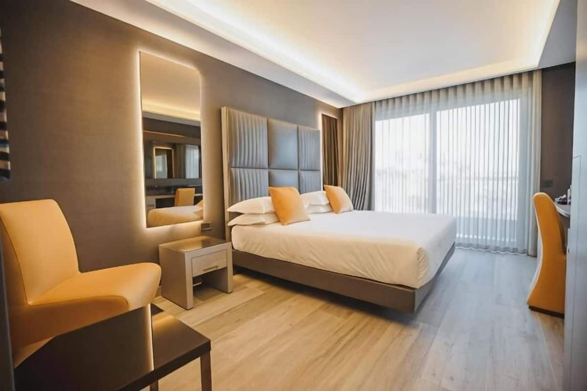 Ein modernes Hotelzimmer mit einem großen Bett, einer Sitzecke, einem Schreibtisch und einem großen Fenster.
