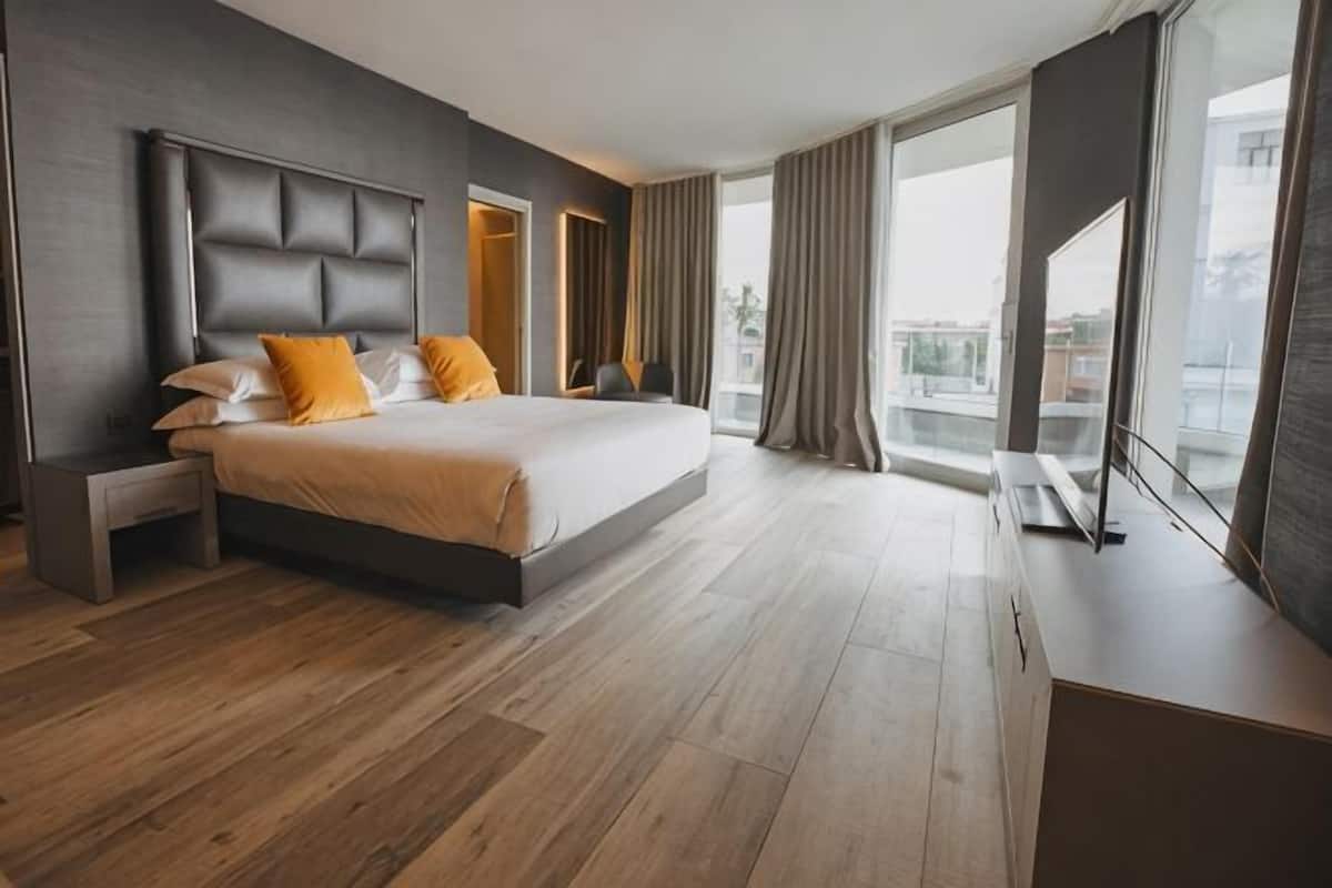 Ein modernes Hotelzimmer mit einem großen Bett, einem Nachttisch, einem Fernseher und einem Balkon mit Vorhängen.