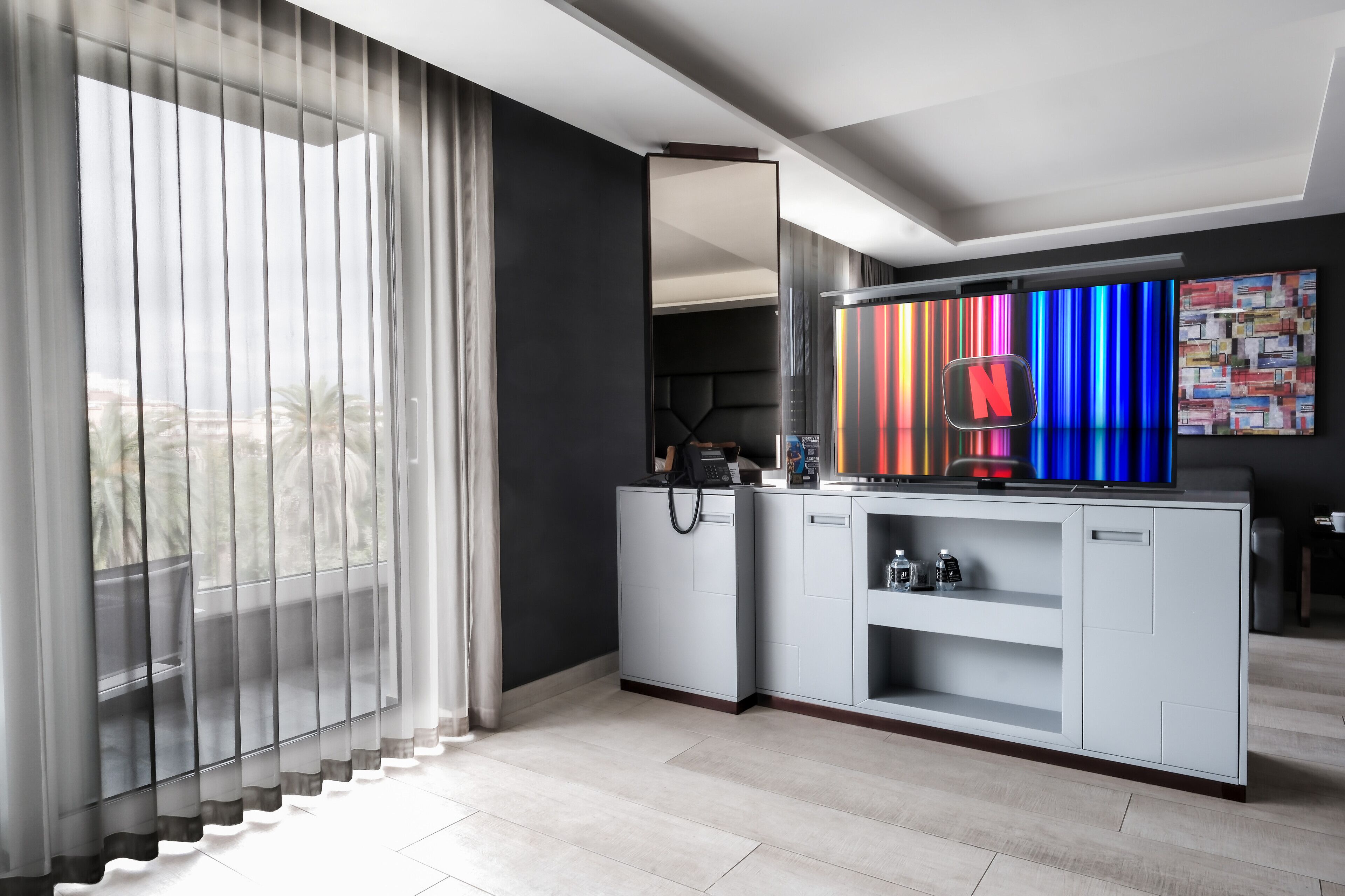 A modern living room with a large window, a TV, and a wall with colorful vertical stripes.