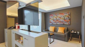 A modern hotel room with a desk, a sofa, a coffee table, and a large abstract painting on the wall.