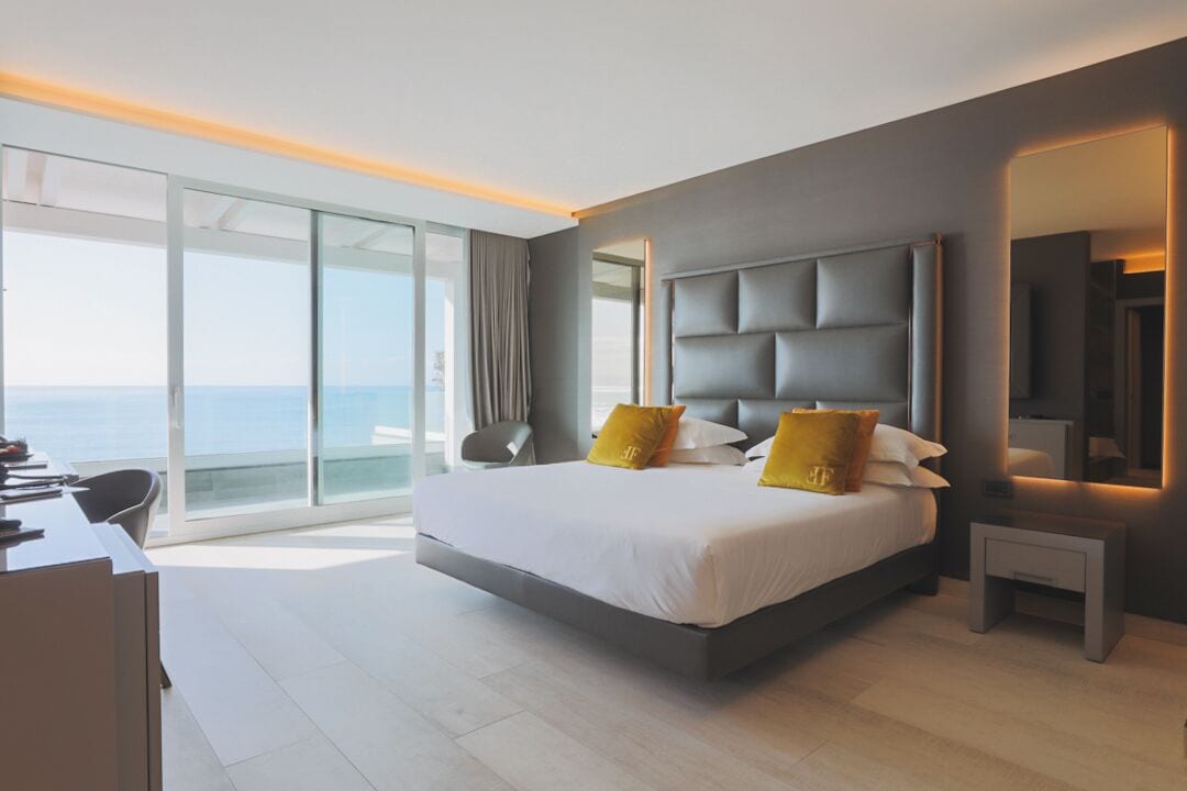 A modern hotel room with a large bed, a desk, and a view of the ocean.