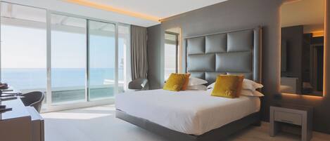 A modern hotel room with a large bed, a desk, and a view of the ocean.