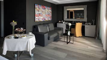 Una sala de estar moderna con un sofá gris, una mesa de comedor con mantel blanco, una mesita auxiliar y un cuadro abstracto grande en la pared.