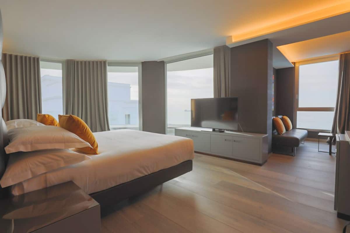 Ein modernes Hotelzimmer mit einem großen Bett, einem Fernseher, einer Couch und einem Schreibtisch.