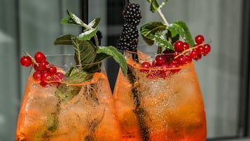 Two cocktails with garnishes, a tray of snacks, and a glass of wine on a white table.