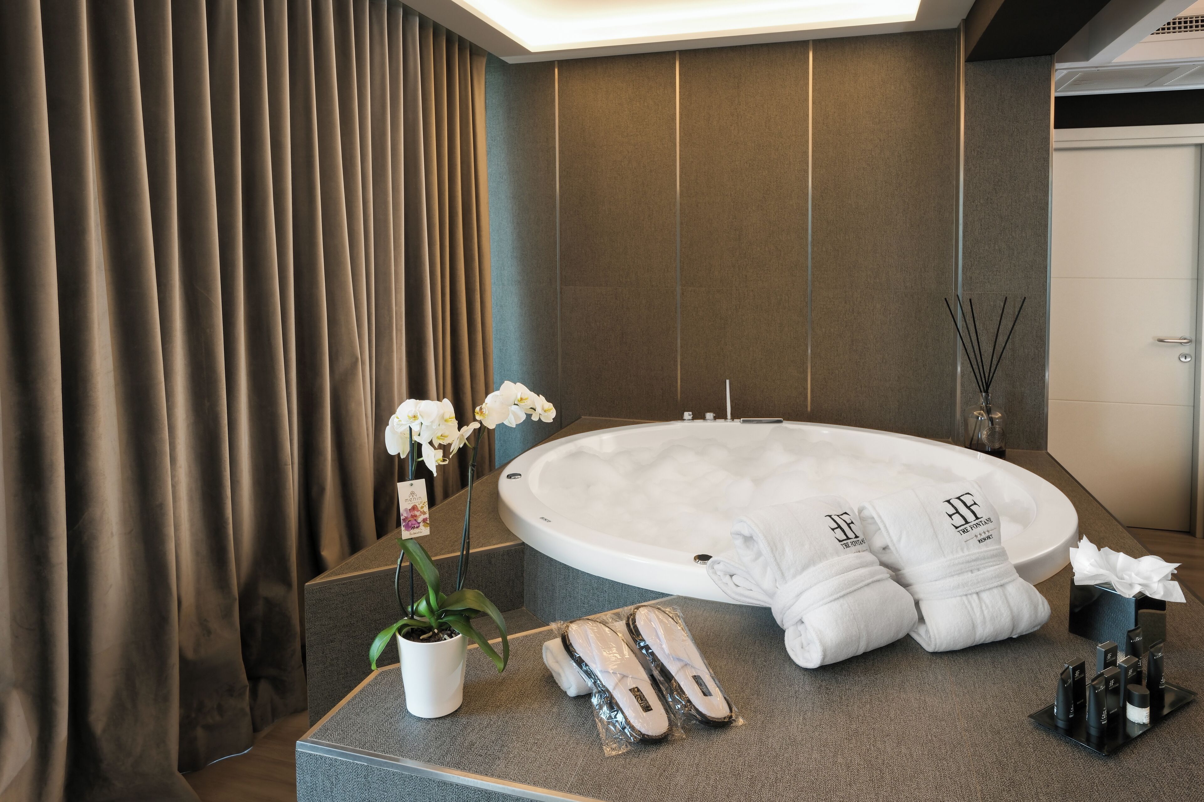 A modern bathroom with a large bathtub, a potted orchid, toiletries, and towels.