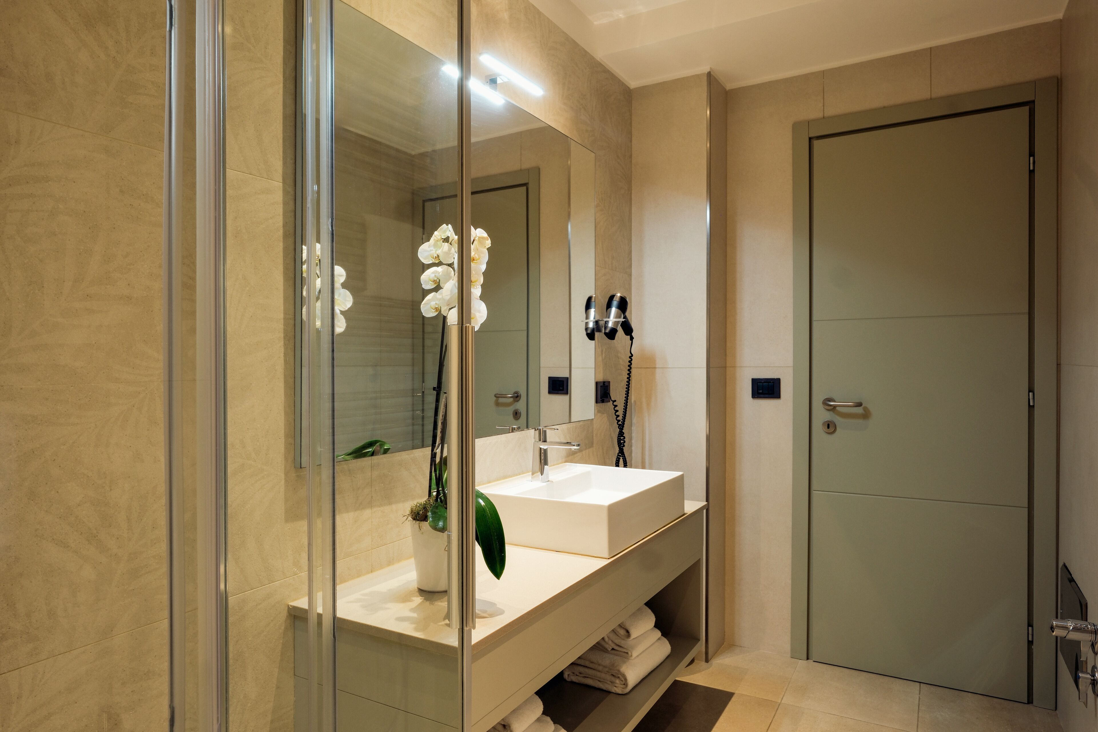 A modern bathroom with a glass shower enclosure, a large mirror, a white sink, and a towel rack.