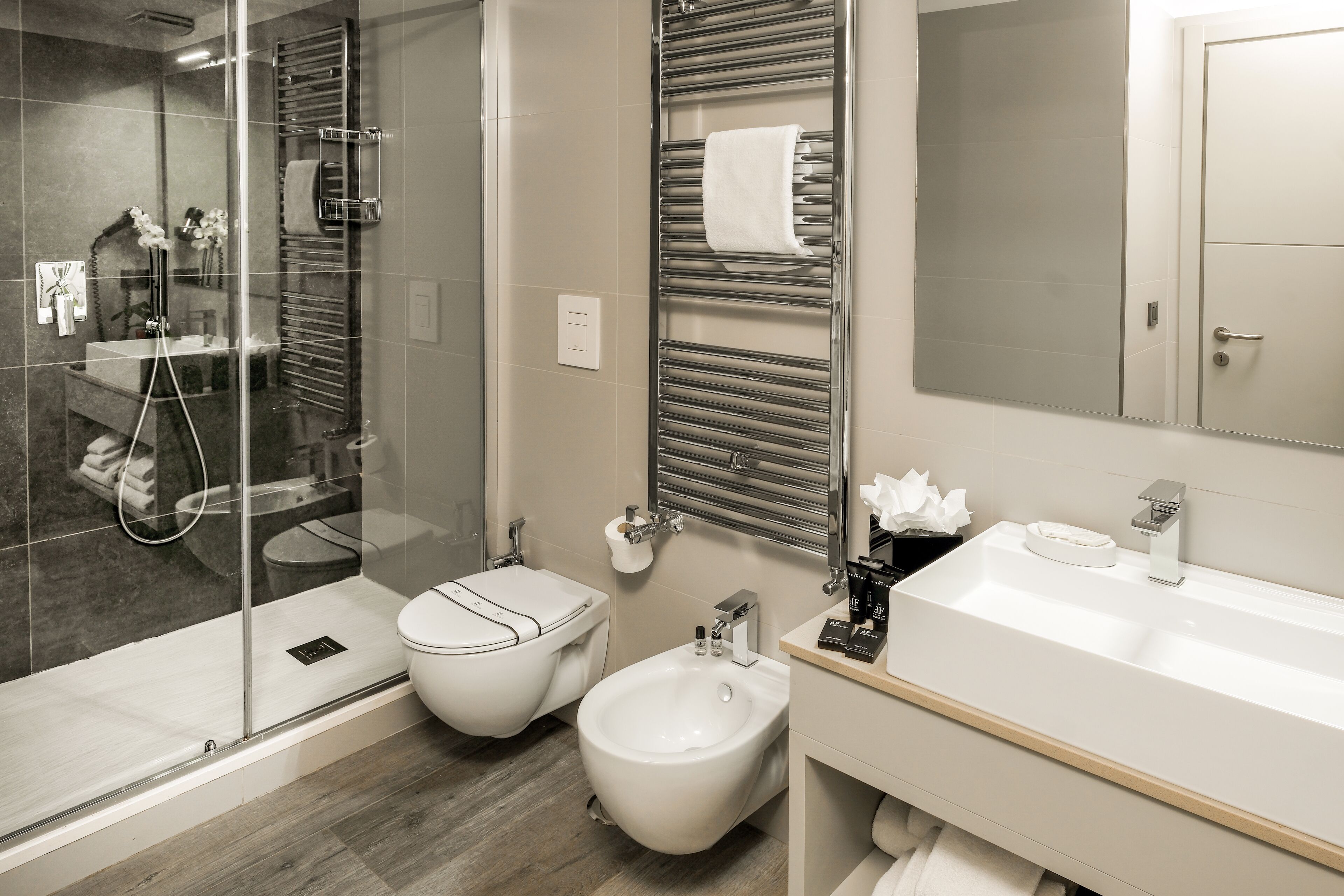 Un baño moderno con ducha de vidrio, un bidé, un inodoro y un lavamanos con espejo superior.