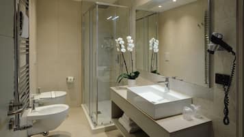 A modern bathroom with a glass-enclosed shower, a white sink, a toilet, and a hairdryer on the wall.