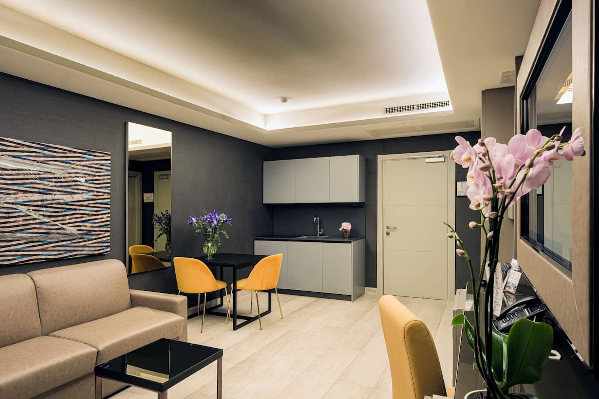 Ein modernes Wohnzimmer mit einer Couch, einem Couchtisch und einem Essbereich mit Stühlen. Es gibt eine Küchenzeile mit Schränken und einer Spüle.