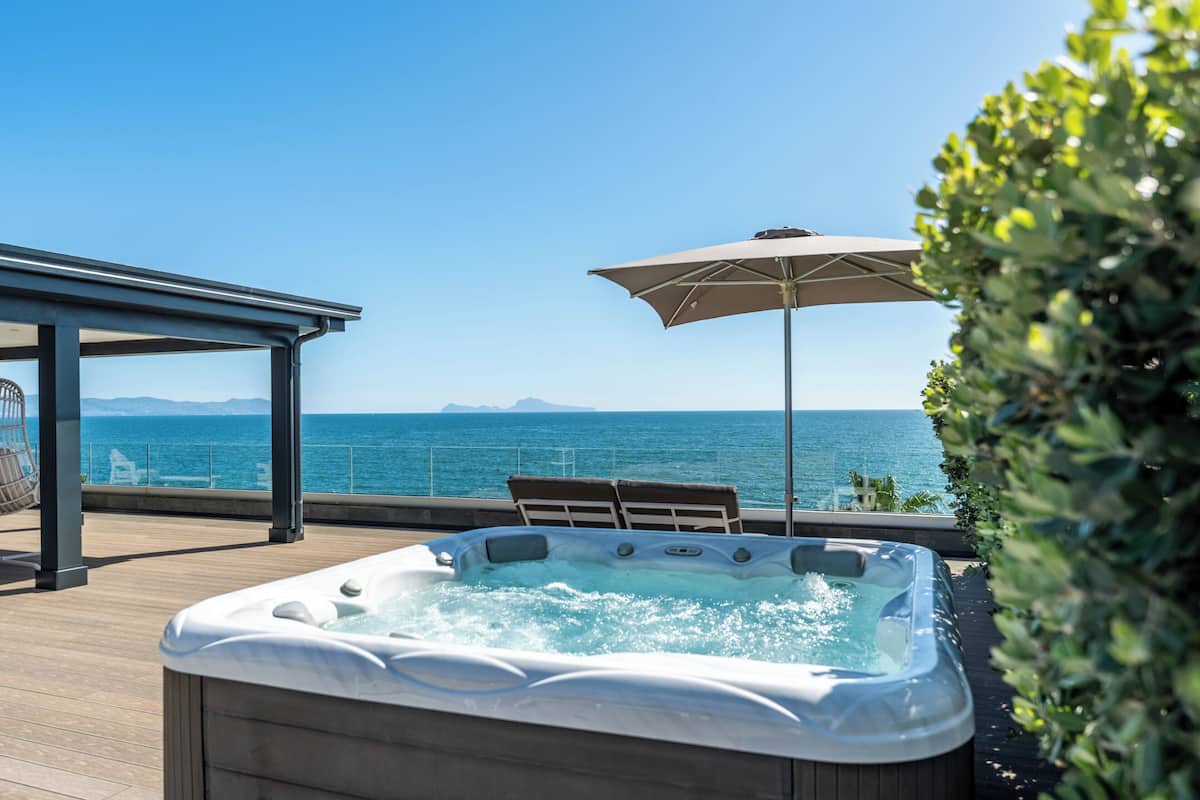 Ein Whirlpool auf einer Terrasse mit Blick auf das Meer, ein überdachter Sitzbereich und ein Sonnenschirm.