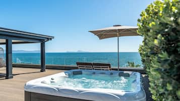 Un jacuzzi en una terraza con vistas al mar, un área de estar cubierta y una sombrilla.