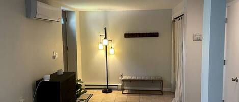 A bedroom with a bed, a dresser, an air conditioner, a floor lamp, and a curtain.