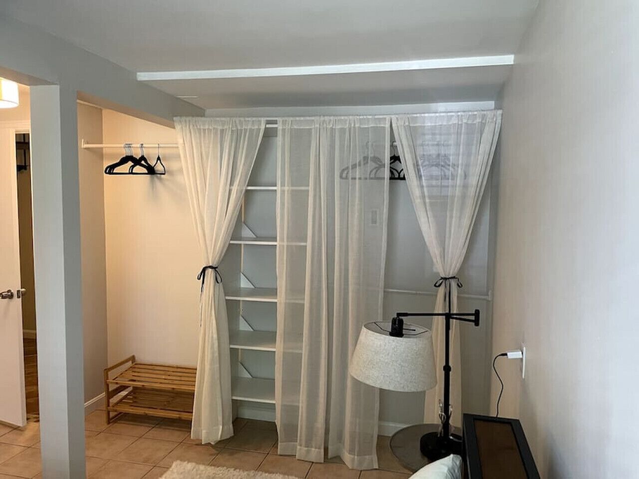 Una habitación con un tendedero de madera, una lámpara y cortinas translúcidas.