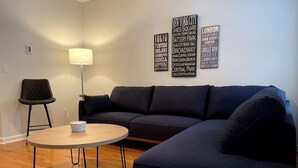 A modern living room with a dark blue sofa, a round coffee table, and a floor lamp. There are wall decorations with city names.