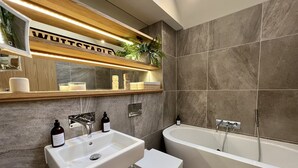 A modern bathroom with a large bathtub, a vanity with a mirror, and a shelf above the sink. - Stunning 3 bedroom beachfront house with extensive sea views (Whitstable)