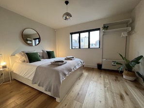 A bedroom with a bed, bedside table, mirror, window, and a potted plant.
