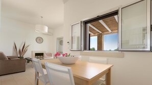 Ein modernes Wohnzimmer mit einem Holzesstisch, weißen Stühlen, einer Couch und einem großen Fenster mit Blick.