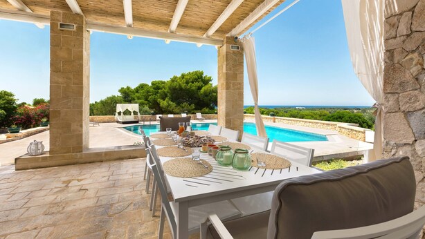 Ein Essbereich im Freien mit Blick auf einen Pool, Steinpfeilern und einer überdachten Terrasse.