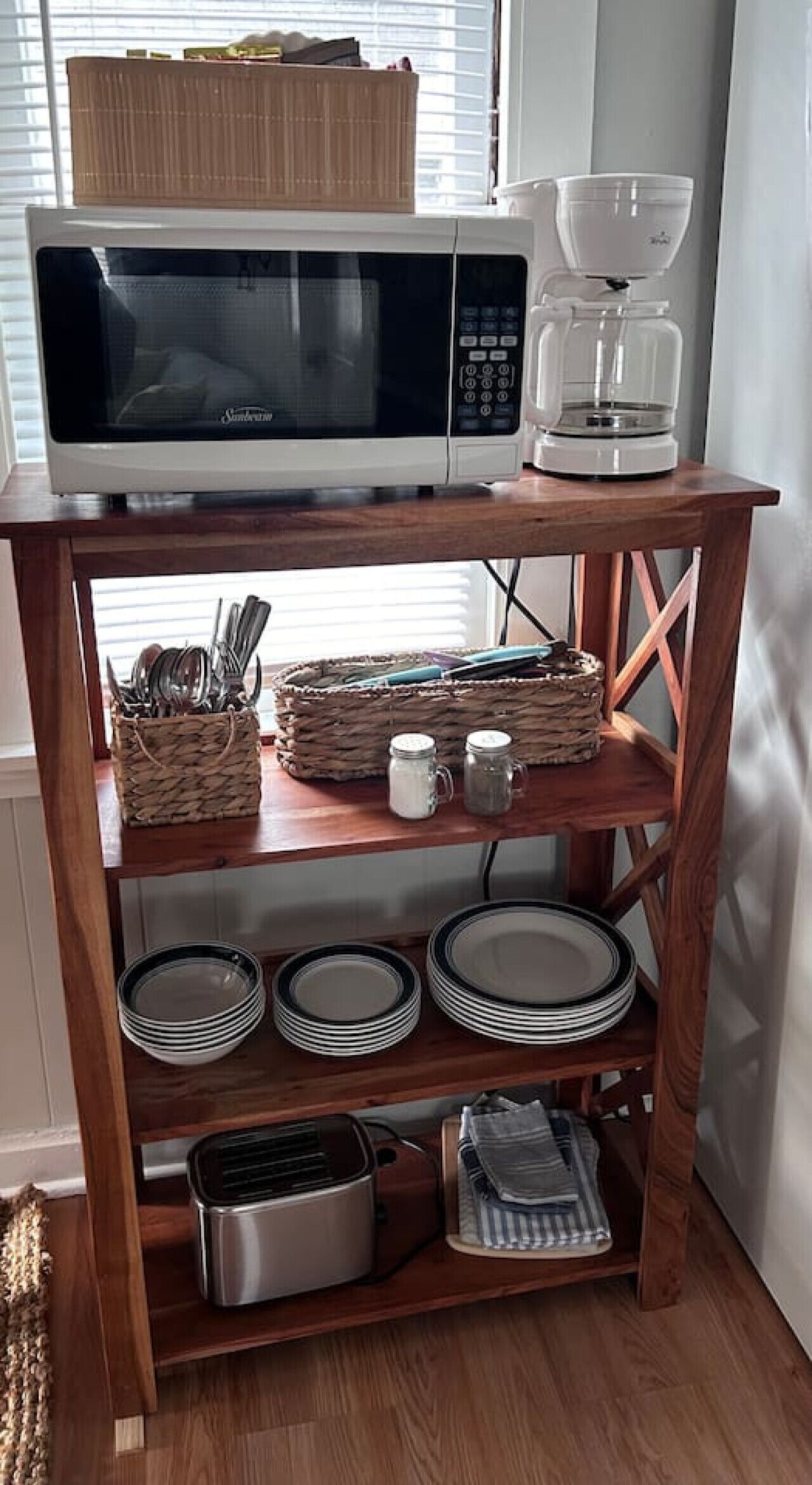Een keuken met een magnetron, koffiezetapparaat en een houten plank met borden, bestek en potten.