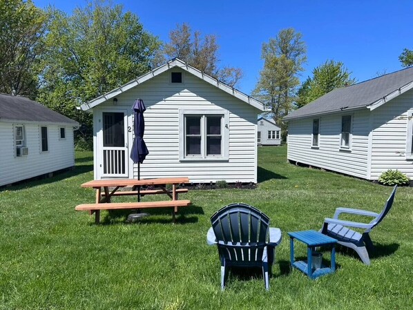 Una cabaña pequeña de un solo nivel con una mesa de picnic y dos sillas Adirondack en el jardín delantero.