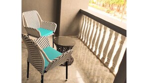 A balcony with two wicker chairs and a small round table, a tiled floor, and a railing with vertical slats.