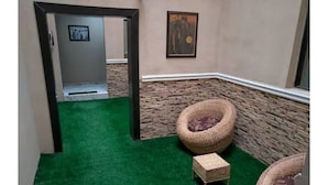 A room with a green carpet, wicker furniture, stone wall, and a painting on the wall.