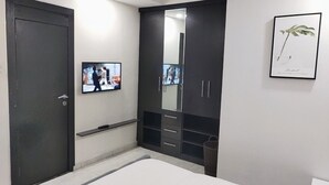 A bedroom with a bed, a wardrobe, a television, and a framed plant.