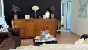 Un salon avec un canapé marron, une table basse avec des magazines, un meuble contenant des objets décoratifs et un lampadaire noir en forme de parapluie.