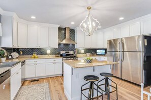 A modern kitchen with white cabinetry, a stainless steel refrigerator, a gas stove, and a chandelier.