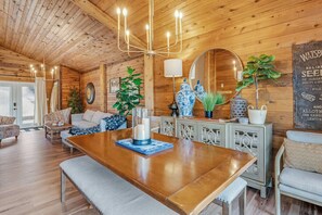 A wooden interior with a dining table, chairs, a chandelier, and decorative items.
