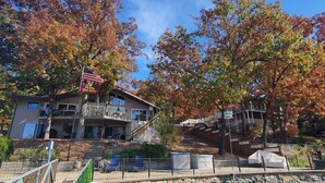 A two-story building with a balcony, a flag, and a stone wall. - BEST LOCATION+ON THE WATER+ROOM FOR EVERYONE! MM23 (Osage Beach)