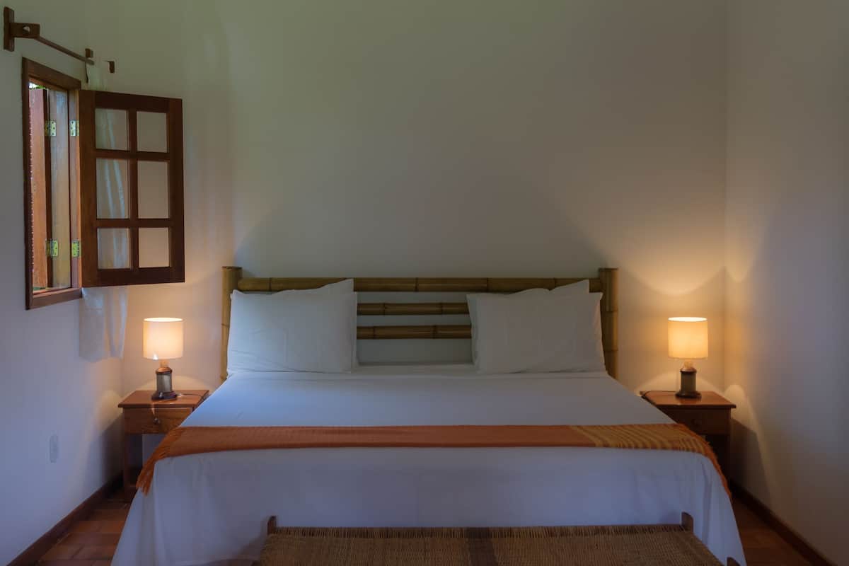 A neatly made bed with a wooden headboard, two bedside lamps, and a bench at the foot of the bed.